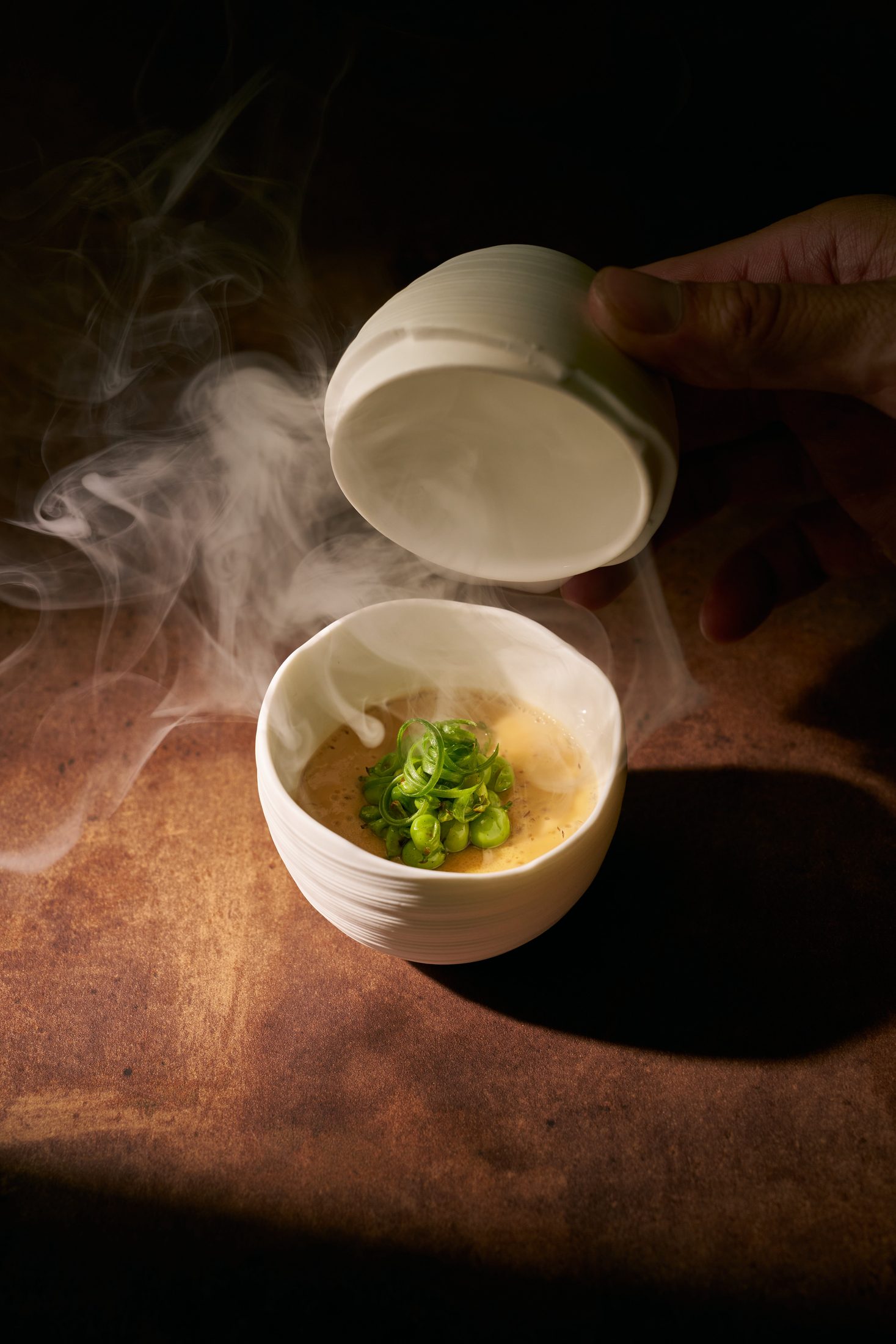 Agedashi prosciutto — prosciutto broth with snap peas, lid lifted at the table
